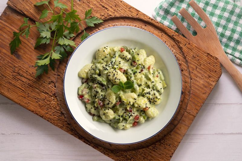 Gnocchi in Yogurt-Asparagus Cream Sauce Dotted with Pomegranate Arils on Bowl on Wooden Tray