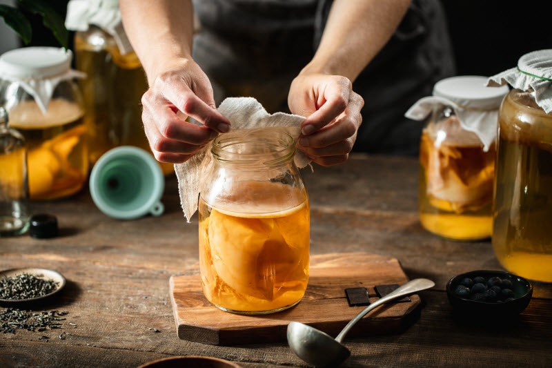 Person Covering Jar of Homemade Kombucha With Cloth to Represent Concept of Gut Health Trends 2025