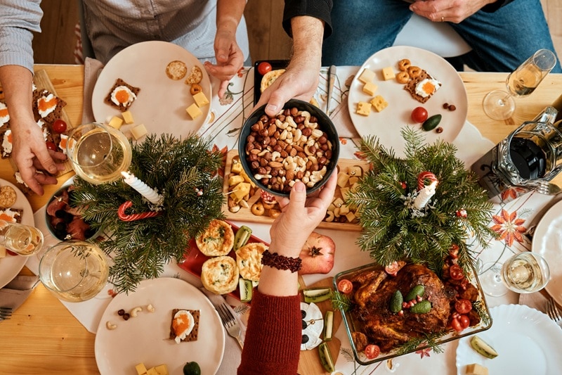 A Bird's Eye View of a Holiday-Themed Table Shows People Passing Mixed Nuts and Filling Their Plates With Other Healthy Holiday Snacks.