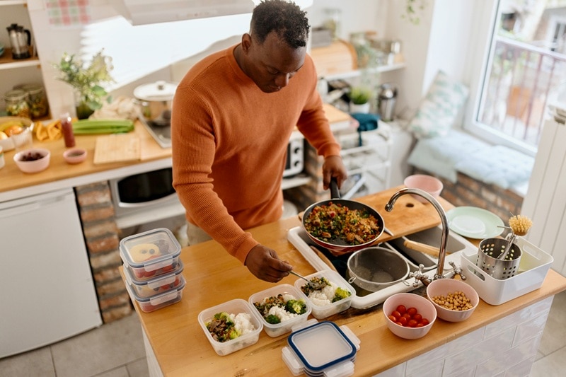 A Man Meal Preps in His Kitchen, Representing How to Stick to a Diet.