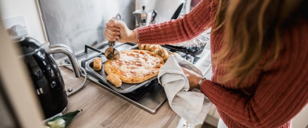 Woman Cutting Frozen Pizza on Stovetop to Represent Concept of Too Much Salt Consumption Linked to Depression