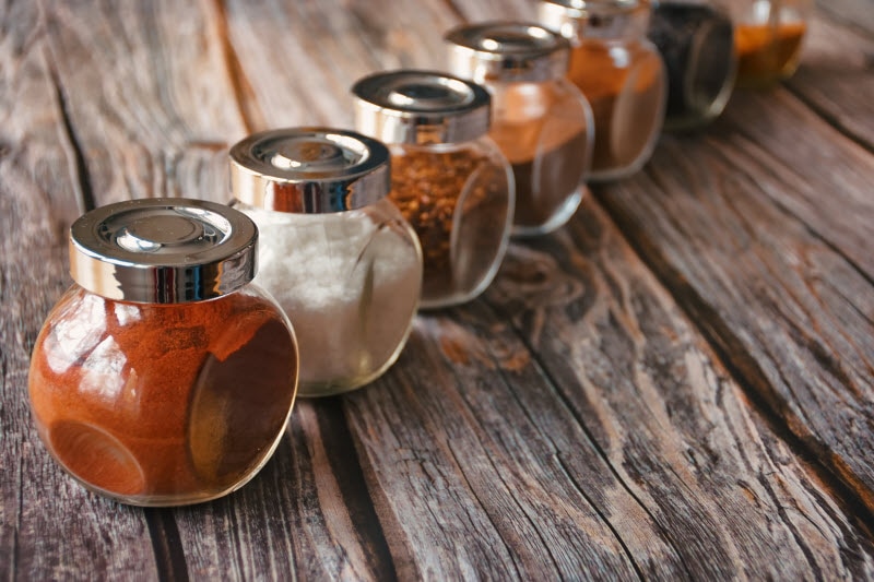 Row of Glass Spice Jars on Wooden Table to Represent Concept of Lead in Food