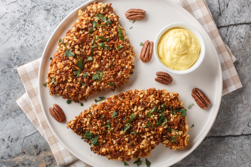 Pecan-Crusted Chicken Breast Sprinkled with Chopped Parsley on a Plate with a Bowl of Honey Mustard Sauce