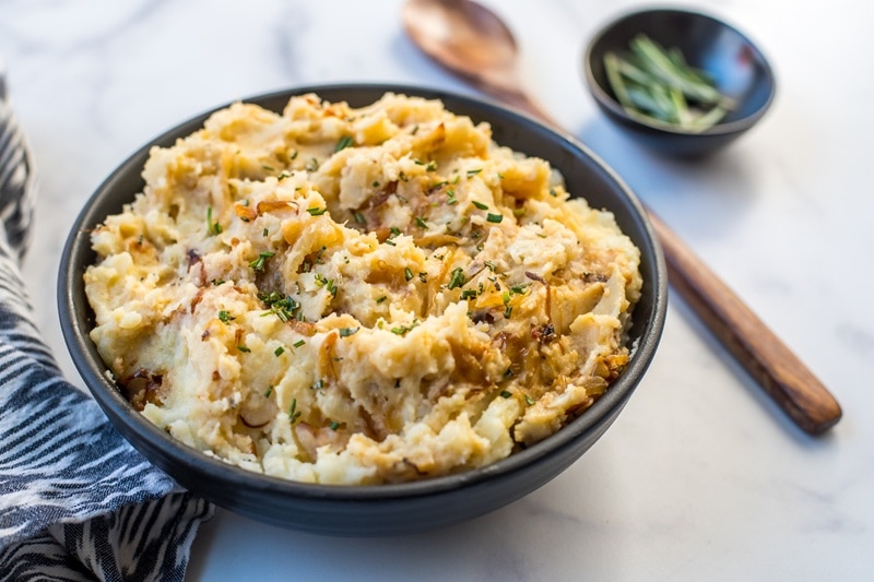 A Creamy Bowl of Rosemary Mashed Potatoes Sits Beside a Wooden Spoon and Fresh Rosemary Sprigs.