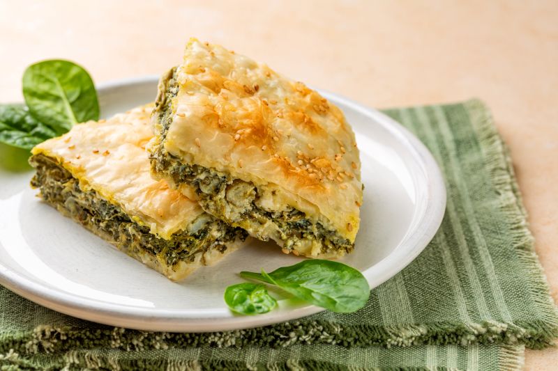Two square slices of Greek spinach pie or spanakopita. The edges are open to expose the spinach and feta filling