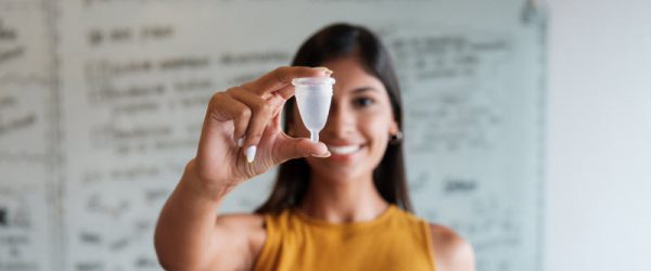 What Are Menstrual Cups - A Complete Guide for Beginners Woman in Yellow Shirt Holding Menstrual Cup to Represent Conceept of What are Mentrual Cups