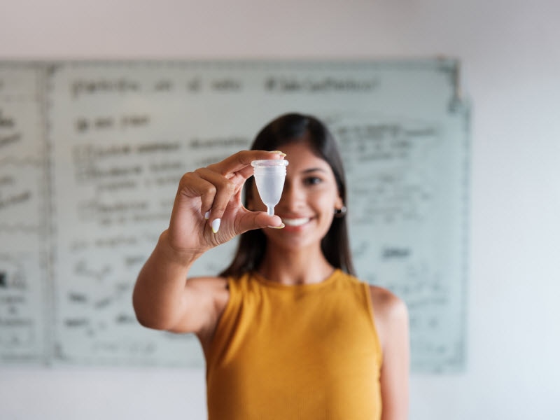 Woman in Yellow Shirt Holding Menstrual Cup to Represent Conceept of What are Mentrual Cups