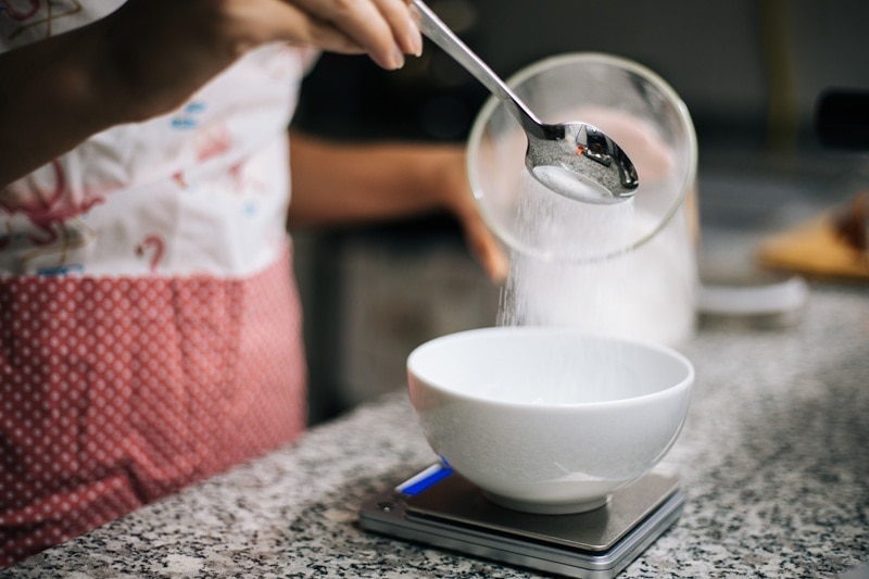 A Woman Pours Allulose Into a Bowl While Baking, Representing the Question, "What is Allulose?"