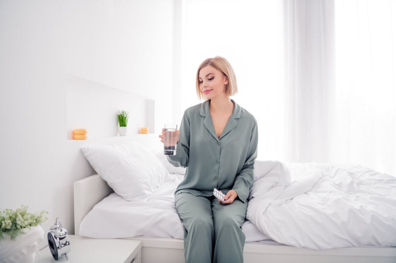 Concept of Taking Supplements on an Empty Stomach Represented by Woman in Bed Taking Vitamins First Thing in the Morning