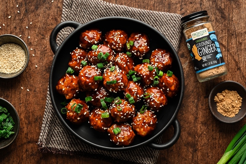 A Black Serving Dish is Filled With Chicken Teriyaki Meatballs and Garnished With Green Onions and Sesame Seeds.
