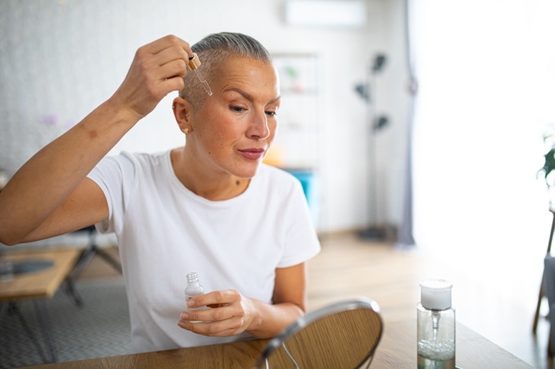 A Woman Applies Skin Care Product to Her Cheek With a Dropper, Representing Ferulic Acid Benefits.