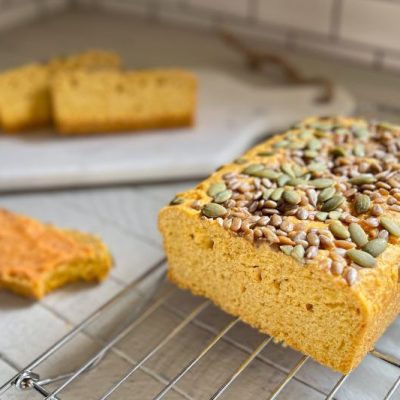 A Loaf of Sliced Chickpea Bread Topped with Sunflower Seeds and Pumpkin Seeds with Sweet Sriracha Compound Butter Sliced Nearby