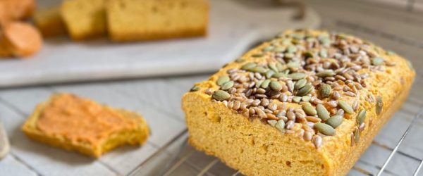 A Loaf of Sliced Chickpea Bread Topped with Sunflower Seeds and Pumpkin Seeds with Sweet Sriracha Compound Butter Sliced Nearby