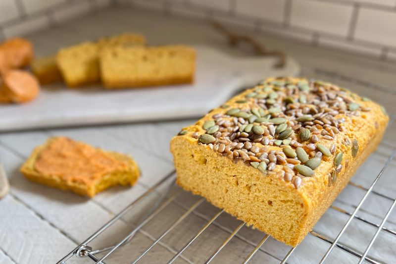 A Loaf of Sliced Chickpea Bread Topped with Sunflower Seeds and Pumpkin Seeds with Sweet Sriracha Compound Butter Sliced Nearby