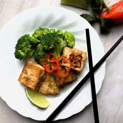 Baked Lemongrass Tofu Cubes on a Plate with Broccoli, Lime and Sliced Red Chili Pepper