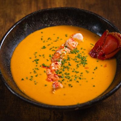 Lobster Bisque Recipe in Round Bowl with Chunks of Lobster and Chopped Chives on Wooden Table