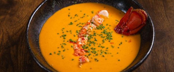 Lobster Bisque Recipe in Round Bowl with Chunks of Lobster and Chopped Chives on Wooden Table