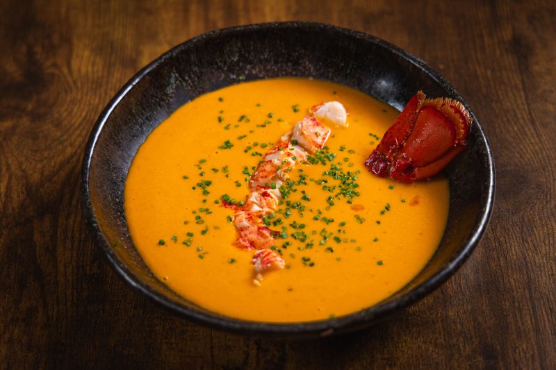 Lobster Bisque Recipe in Round Bowl with Chunks of Lobster and Chopped Chives on Wooden Table