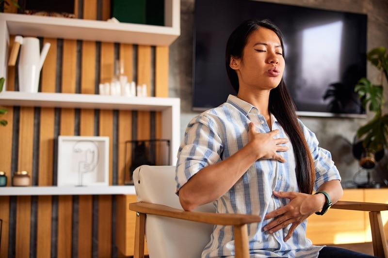 A Young Woman Performs Seated Breathing Exercises While Seated, Representing Natural Energy Boosters.