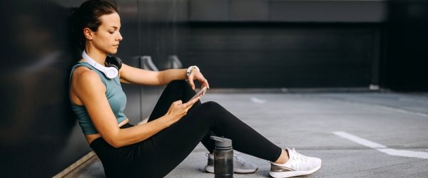 A Woman in Workout Clothes Sits and Reviews Information on Her Phone, Representing a Personalized Workout Program Created by AI.