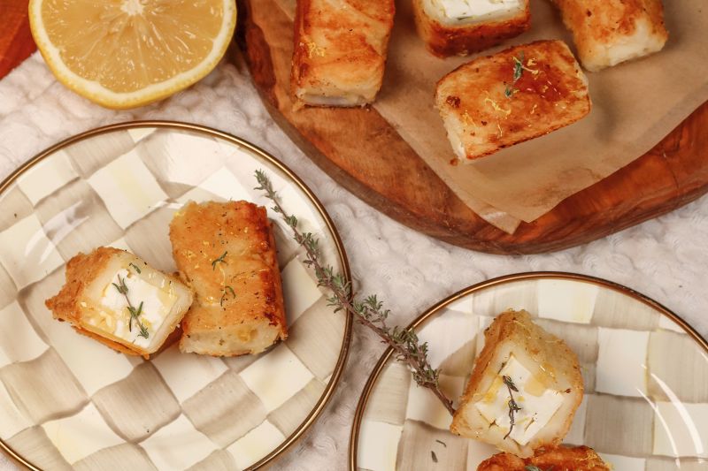 Crispy, flaky phyllo wrapped around warm, tangy feta cheese on appetizer plates, drizzled with honey and sprinkled with flaky salt