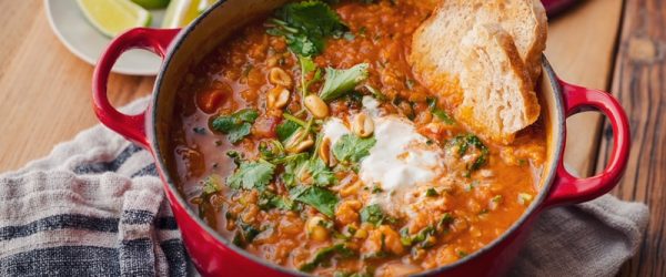 A Red Cast Iron Pot is Filled With African-Inspired Red Lentil Stew and Topped With a Dollop of Yogurt, Fresh Herbs and Two Slices of Bread for Dipping.