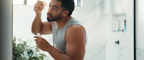 A Man Applies a Serum While Looking in the Mirror, Representing the Idea of Skin Training to Apply Active Ingredients.