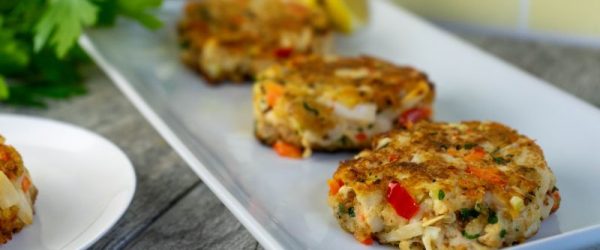 Vegan Crab Cakes Laid Out in a Row on a Rectangular Serving Plate with Lemon Wedges