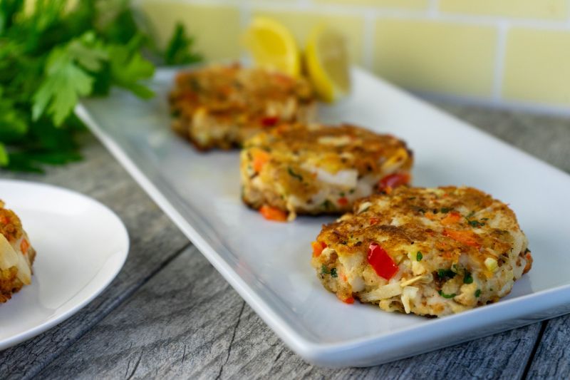Vegan Crab Cakes Laid Out in a Row on a Rectangular Serving Plate with Lemon Wedges