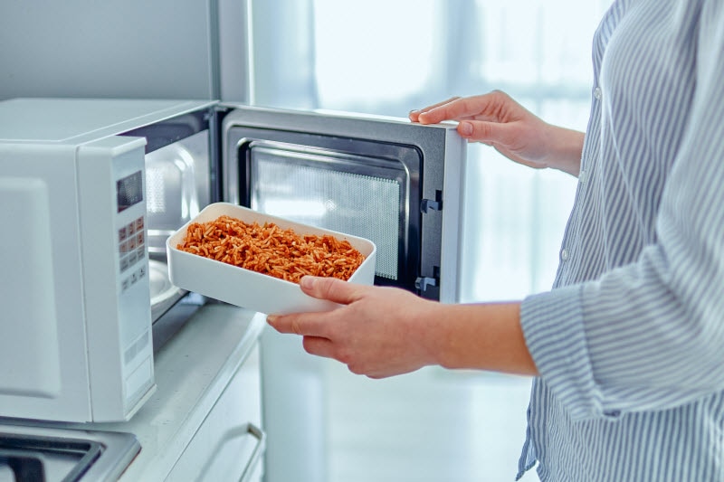 Torso View of Woman Heating Up Food After Learning What Not to Put in a Microwave