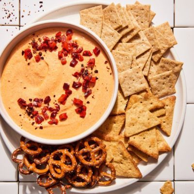 Whipped Feta Dip Topped with Pimentos in a Bowl on a Serving Platter Filled with Crackers and Pretzels