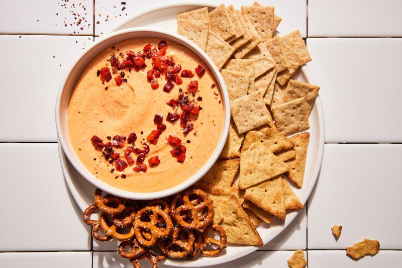Whipped Feta Dip Topped with Pimentos in a Bowl on a Serving Platter Filled with Crackers and Pretzels