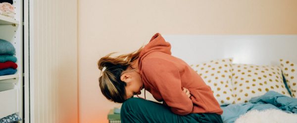 Woman Suffering From Period Flu Hunched Over in Pain on Side of Bed