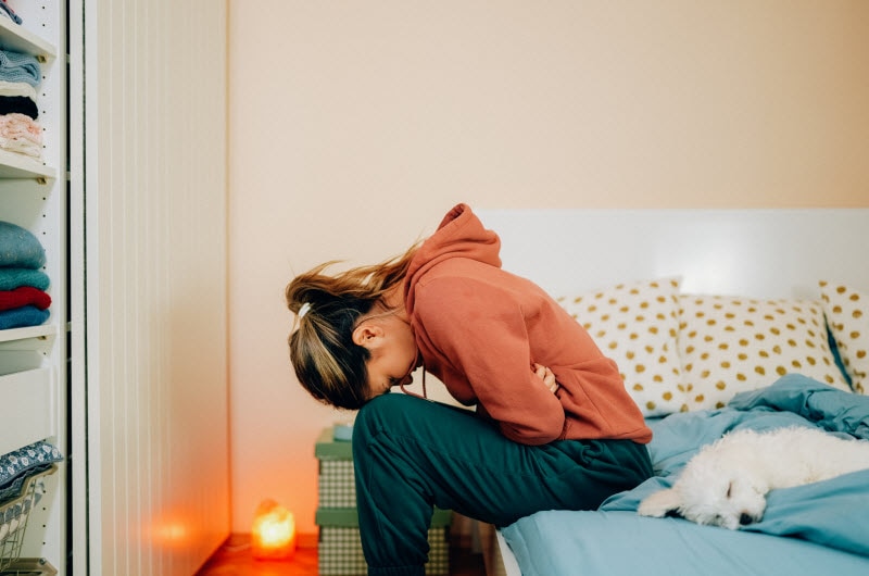 Woman Suffering From Period Flu Hunched Over in Pain on Side of Bed