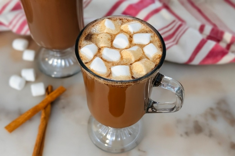 A Glass Mug Is Filled to the Brim With Protein Hot Chocolate and Topped With Mini Marshmallows.
