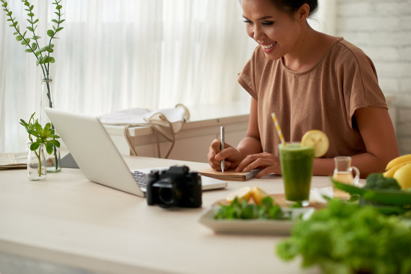 Woman Surrounded by Healthy Food Researching New Dietary Guidelines for Americans on Her Laptop at Desk